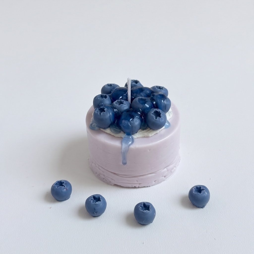 SORA SCENT Mini Blueberry Mousse Cake Candle on a clean background, showcasing its pastel lilac smooth cylinder base, white frosted soy cream, and detailed dark blue wax blueberries with dripping glaze.