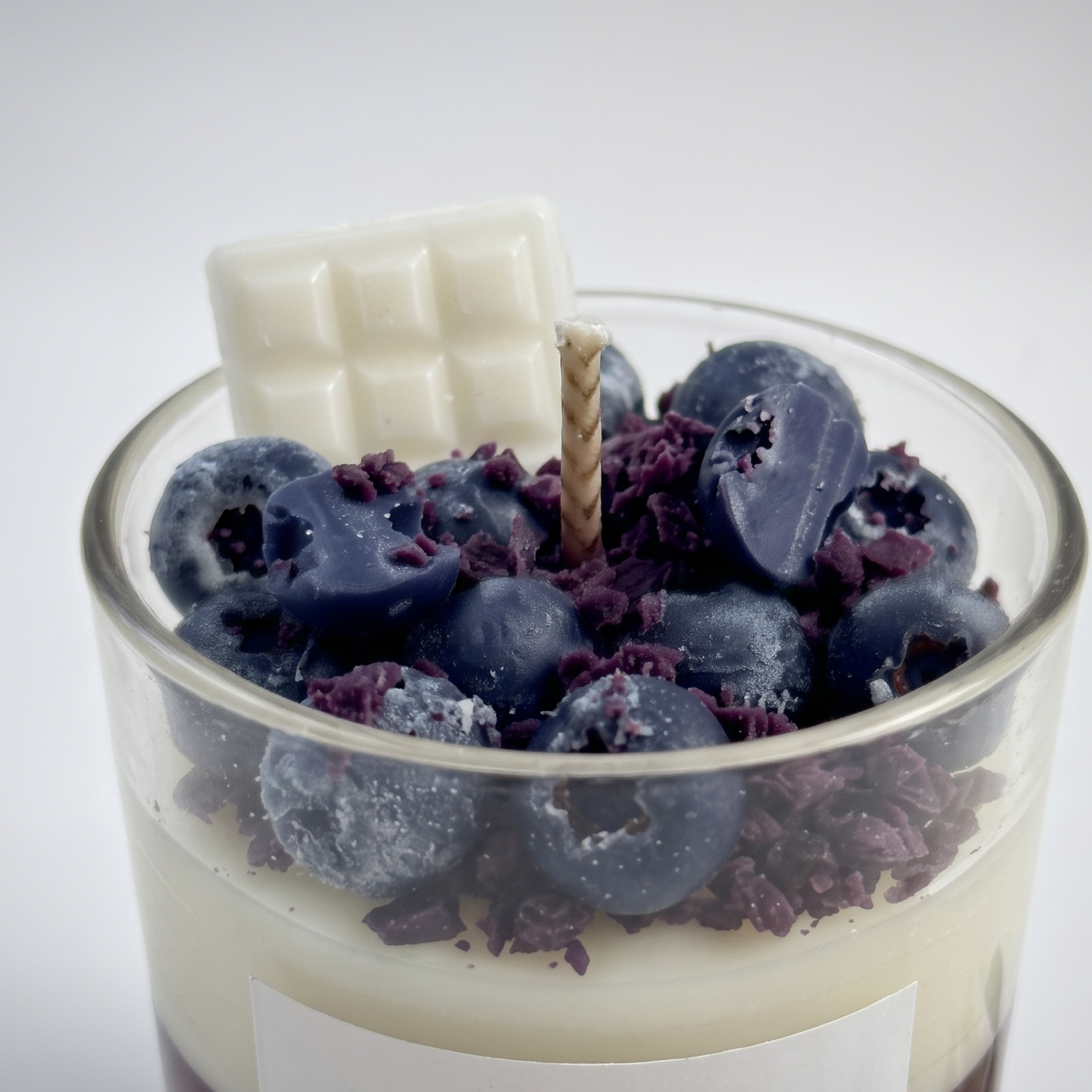 Macro close-up of SORA SCENT's Blueberry White Chocolate Parfait Candle, highlighting the realistic frosted texture of the wax blueberries, purple crumbs, and white chocolate bar topper.