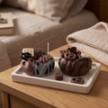 shows two handcrafted Mini Chocolate Glazed Donut Candles by SORA SCENT sitting on a white tray on a wooden nightstand, featuring realistic wax pretzels, mini waffles, and chocolate shavings.