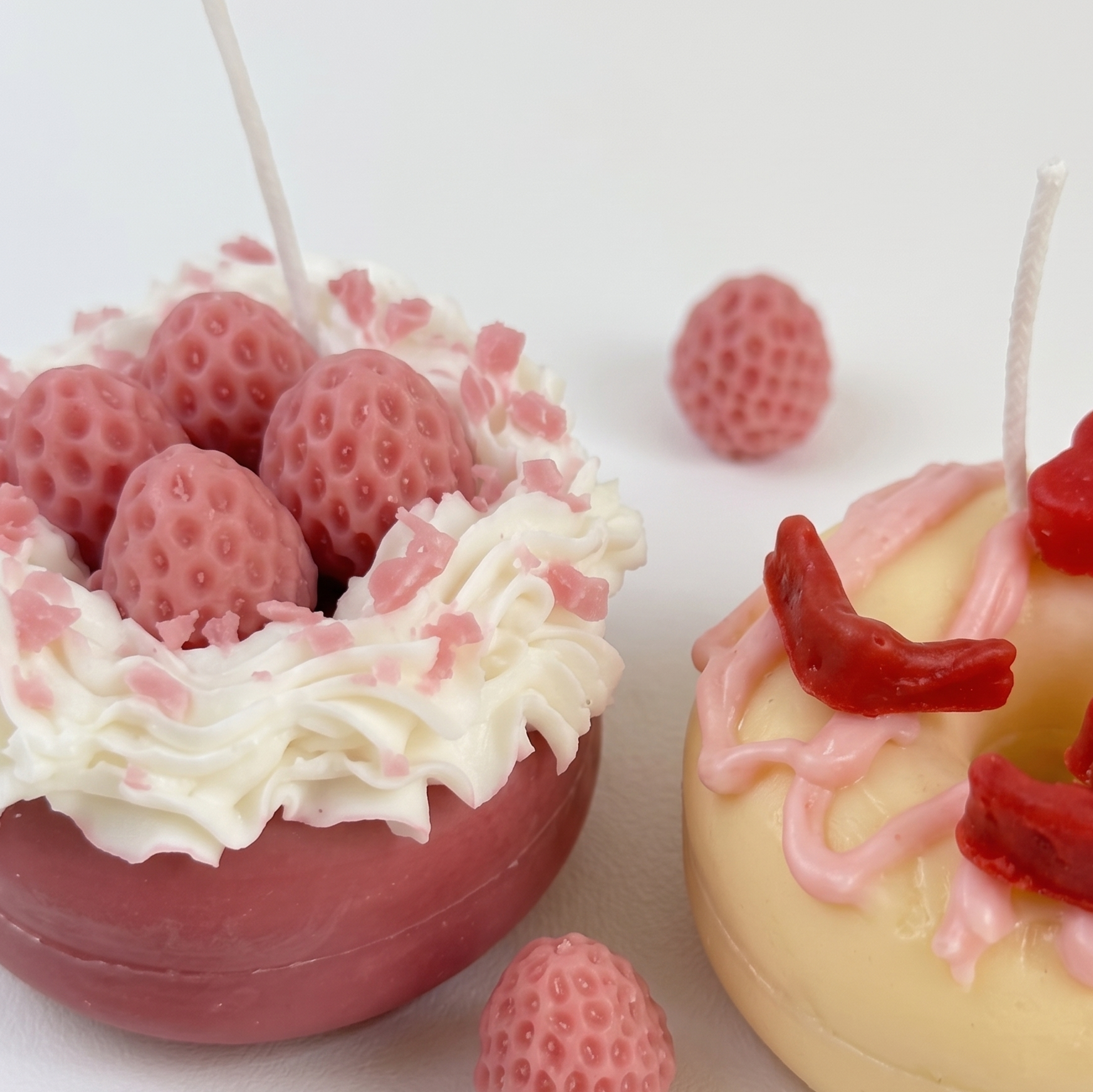 Macro close-up of SORA SCENT's Mini Pink Strawberry Donut Candle, highlighting the detailed seed texture of the pink wax strawberries and white cream piping.