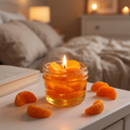 shows a handcrafted Sweet Mandarin Marmalade Candle by SORA SCENT in a glass jar on a marble kitchen island, filled with golden translucent jelly wax and realistic wax mandarin segments, next to a small ceramic plate with more loose wax orange slices.