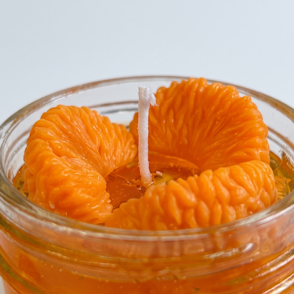 shows a handcrafted Sweet Mandarin Marmalade Candle by SORA SCENT in a glass jar on a marble kitchen island, filled with golden translucent jelly wax and realistic wax mandarin segments, next to a small ceramic plate with more loose wax orange slices.