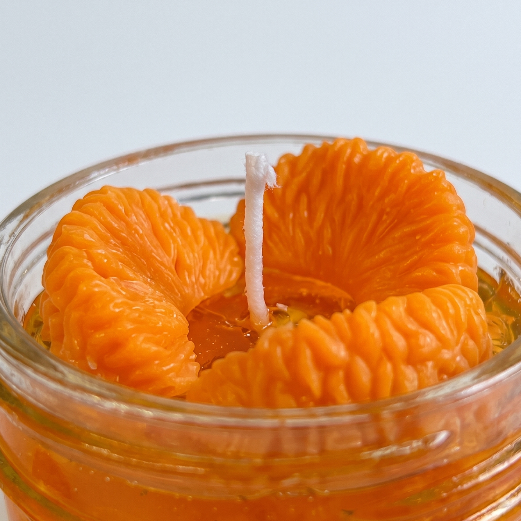 shows a handcrafted Sweet Mandarin Marmalade Candle by SORA SCENT in a glass jar on a marble kitchen island, filled with golden translucent jelly wax and realistic wax mandarin segments, next to a small ceramic plate with more loose wax orange slices.