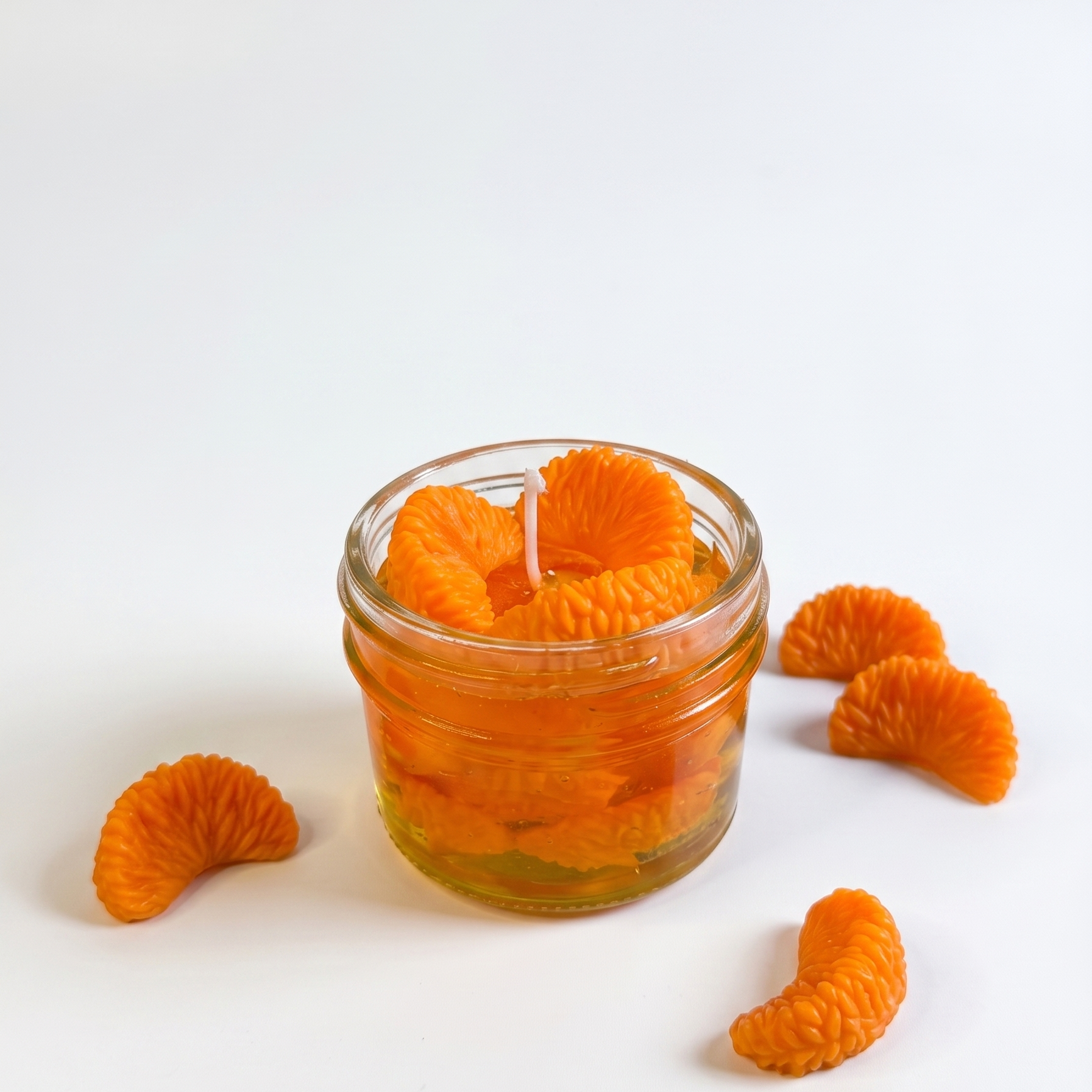 shows a handcrafted Sweet Mandarin Marmalade Candle by SORA SCENT in a glass jar on a marble kitchen island, filled with golden translucent jelly wax and realistic wax mandarin segments, next to a small ceramic plate with more loose wax orange slices.