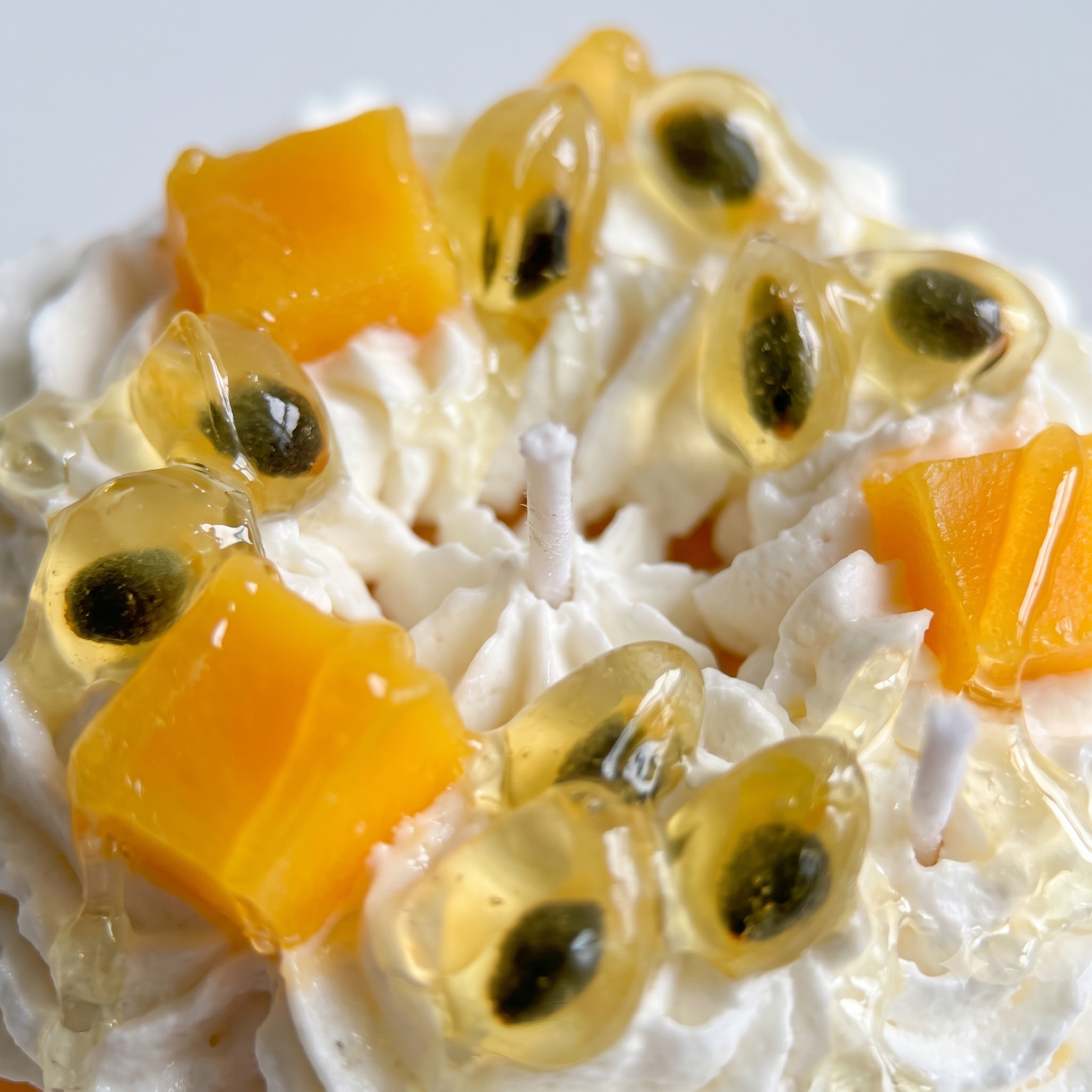 Macro close-up of SORA SCENT's Passion Fruit Macaron Candle, highlighting the detailed seed texture of the wax passion fruit, mango cubes, and shimmering dripping syrup.