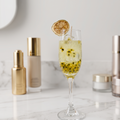 Lit Malibu Sunshine Spritz Candle in a champagne flute on a wooden window sill, capturing warm sunset golden hour light filtering through the glass and illuminating the sparkling bubbles and suspended fruit seeds in the gel wax.