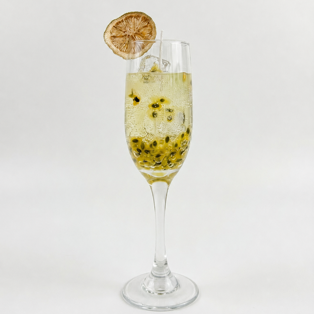 Handcrafted Malibu Sunshine Spritz Candle by SORA SCENT in an elegant glass champagne flute on a clean white background, featuring pale golden sparkling gel wax with realistic bubbles, floating wax passion fruit seeds, and a dehydrated lemon slice garnish.