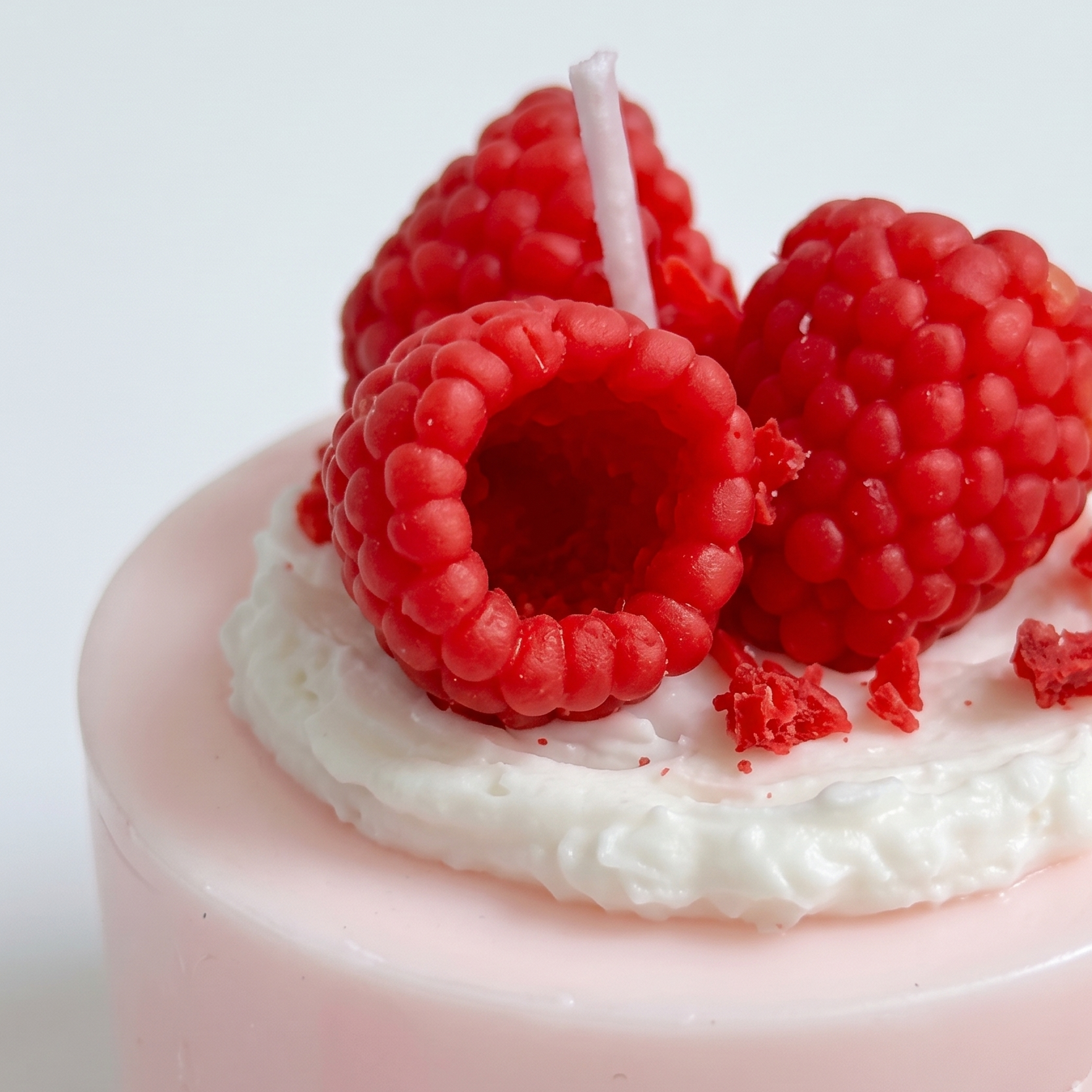 Macro close-up of SORA SCENT's Mini Raspberry Mousse Cake Candle, highlighting the intricate hollow-center seed texture of the wax raspberries and white cream crumbs.
