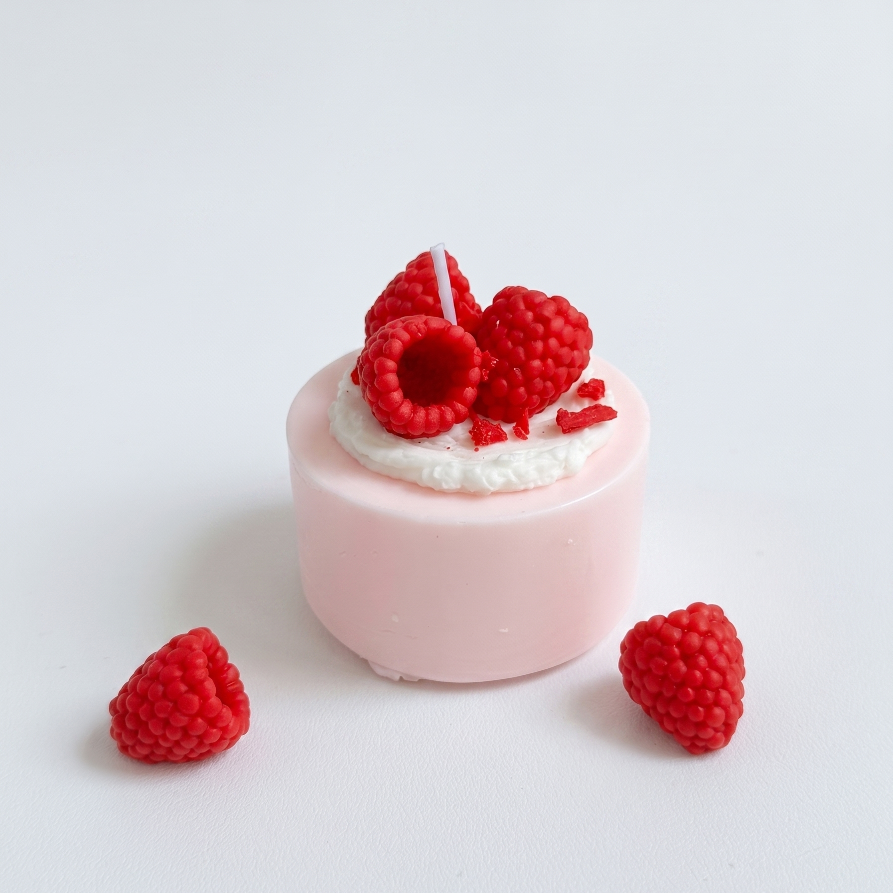 SORA SCENT Mini Raspberry Mousse Cake Candle on a clean background, showcasing its pastel pink smooth cylinder base, white frosted soy cream, and detailed red wax raspberries.