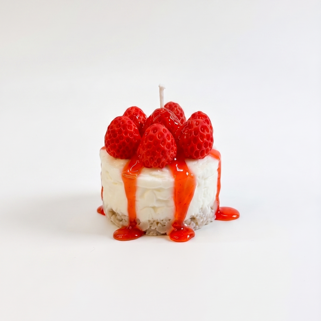shows a hyper-realistic, handcrafted Mini Strawberry Cheesecake Candle by SORA SCENT standing on a minimalist wooden coffee table in soft sunlight, featuring a textured crumb crust base, a smooth white cream layer, dripping red strawberry glaze, and realistic red wax strawberries on top, with a blurred book in the background.